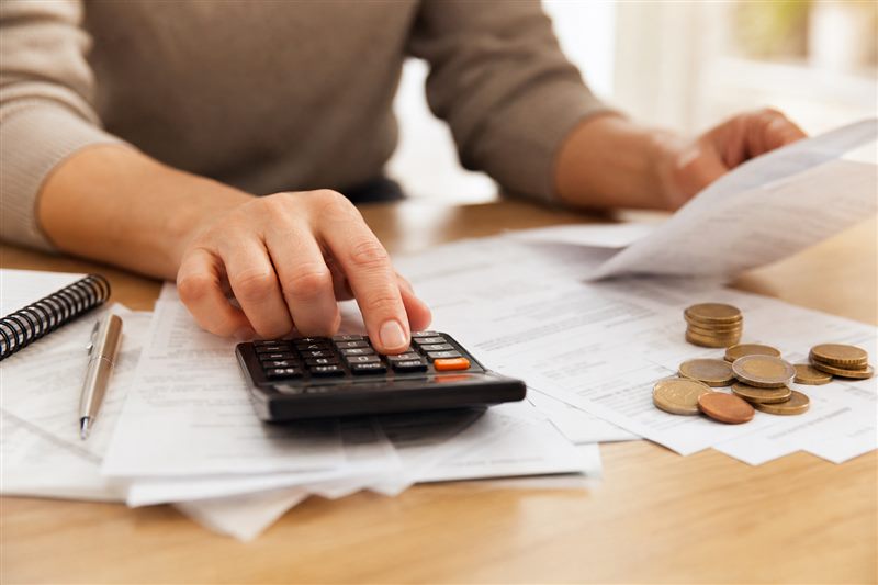 Hands using a calculator alongside household bills and euro coins for budget planning